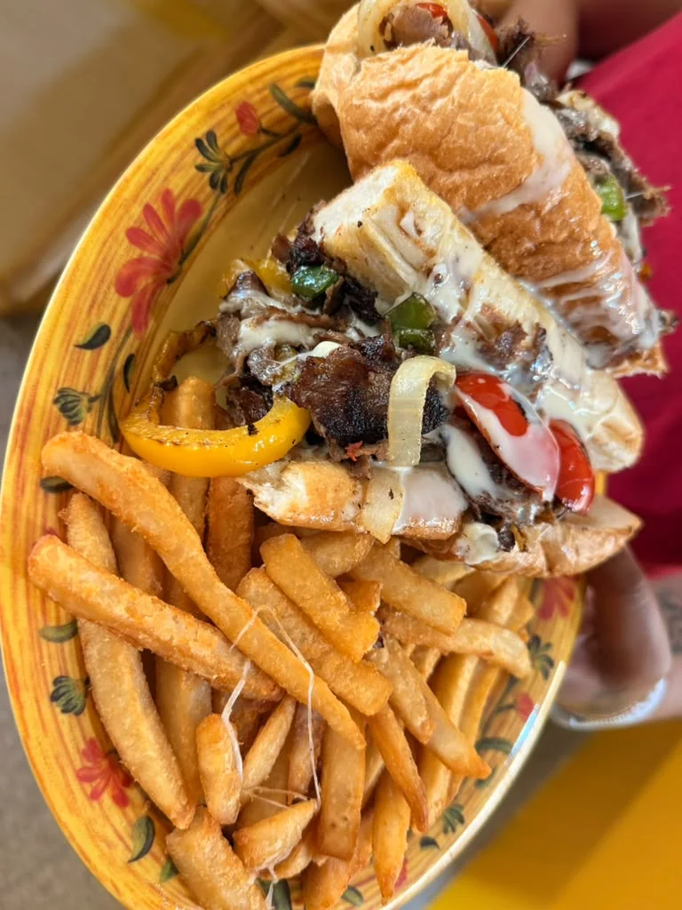 Philly cheesesteak served with fries on a yellow plate